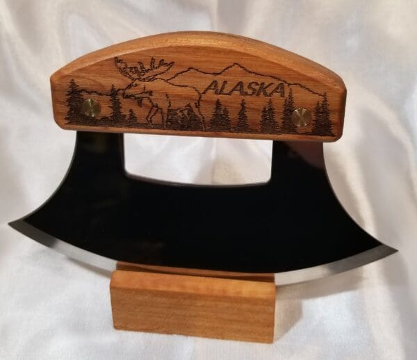 A wooden ulu with an alaskan scene on it.